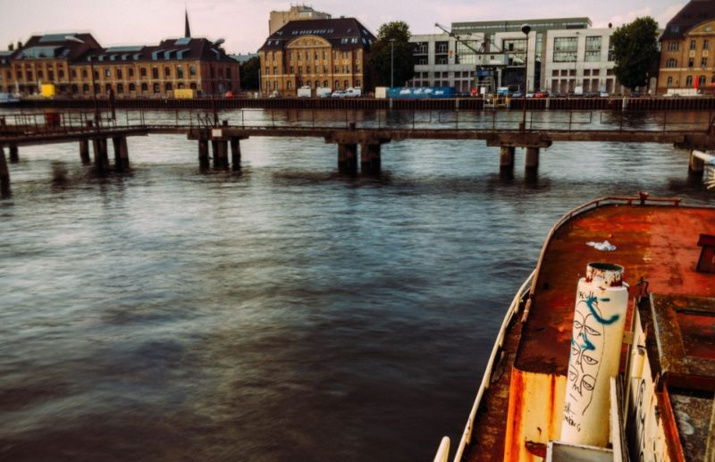 The abandoned boat in the Spree River has a name, even though I couldn’t find one when Fotostrasse visited the place back in July 2016. The boat is called MS Dr. Ingrid Wengler. It was named after the owner’s true love, a surgeon at the Dreifaltigkeits-Hospital in Lippstadt. She died in 1979 and she left a hole that never closed. This is why Franz Günther van de Lücht, the owner of the abandoned boat, says about his loss. But the fact that the boat that carries her name is stuck between the Molecule Man sculpture and Badeschiff leaves another one.