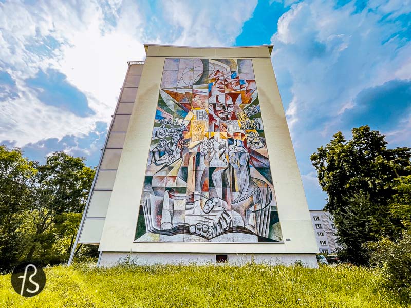 This Lenin mural in Halle Neustadt was unveiled in 1971 by Erich Enge, a bricklayer by training who found himself in large format paintings. His mural is named %22He stirred the sleep of the world%22 and visually presents the three essential reforms that Lenin initiated in the Soviet Union. First, with the elimination of illiteracy, followed by a country comprehensive land reform and the country's electrification in the 1920s. All these elements are presented around Lenin's face in the mural, surrounded by young people reading and learning.